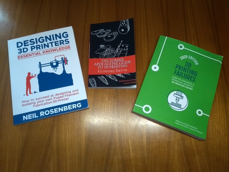 Three books on a table: Designing 3D Printers by Neil Rosenberg, The Zombie Apocalypse Guide to 3D Printing by Clifford Smyth, and 3D Printing Failures by Sean Aranda.